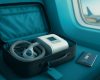 Open carry-on suitcase with CPAP machine and mask on a teal seat beside an airplane window; Indian passport nearby.