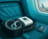 Open carry-on suitcase with CPAP machine and mask on a teal seat beside an airplane window; Indian passport nearby.
